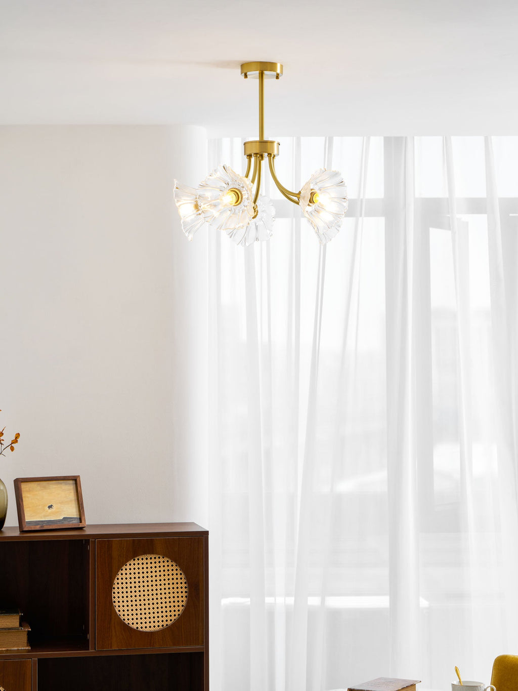 A rattan cabinet and a framed photo sit near a sheer curtain beneath this Clérachic chandelier.