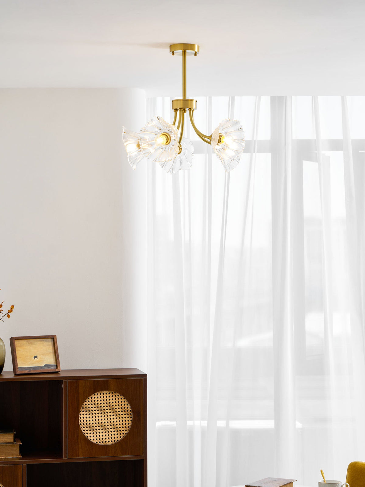 A rattan cabinet and a framed photo sit near a sheer curtain beneath this Clérachic chandelier.