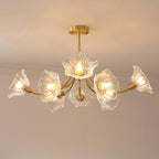 Brass arms hold ruffled glass petal shades lit warmly on this Clérachic chandelier against a plain wall.
