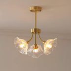 Warm light glows from this Clérachic chandelier's glass petal shades, hung in the corner of a softly lit room.