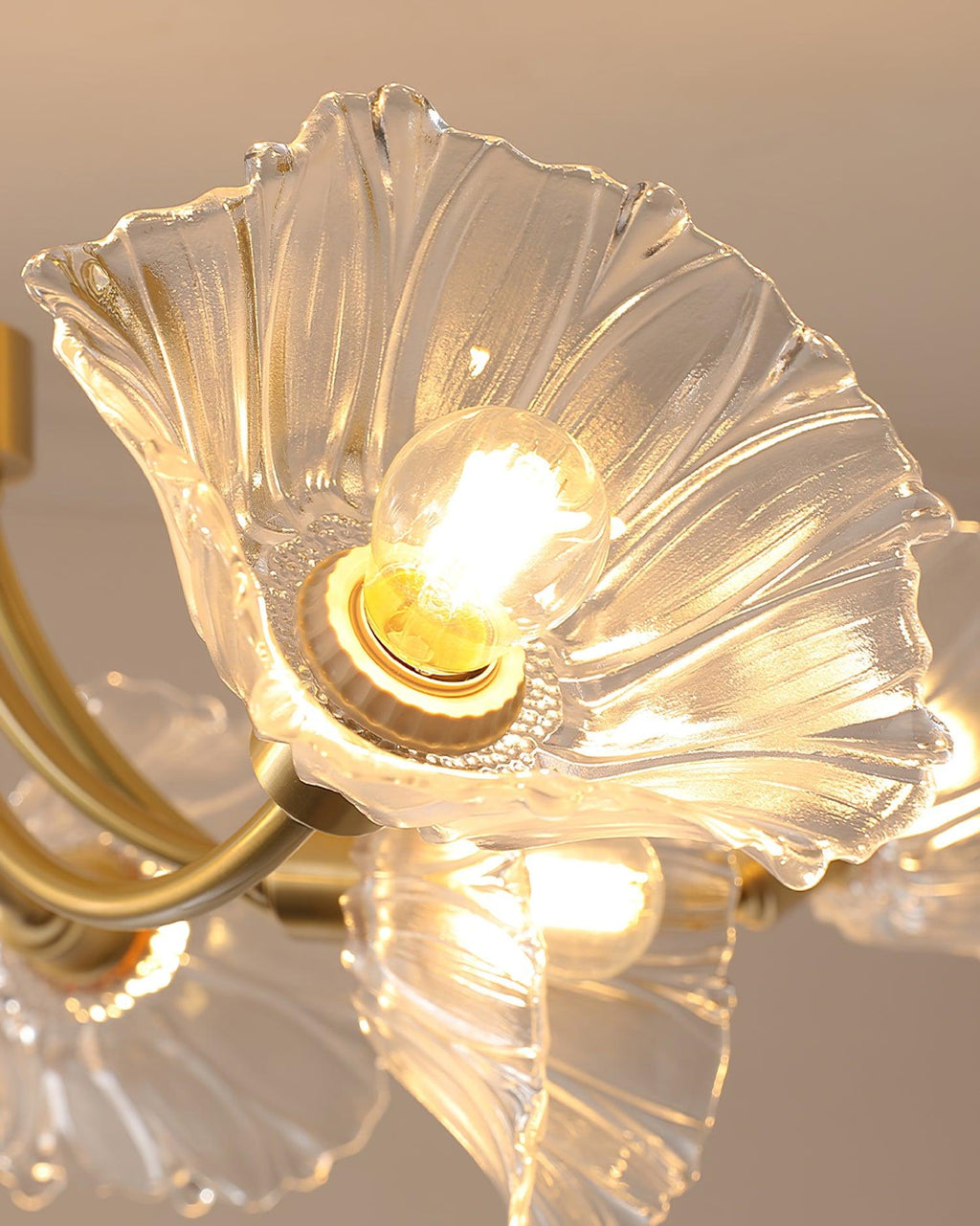 Close view of several ruffled glass petal shades fanning from the brass frame of this Clérachic chandelier, lit warmly.