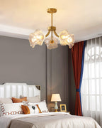In a grey bedroom with a striped curtain and a lit bedside lamp, this Clérachic chandelier's petal shades glow softly.
