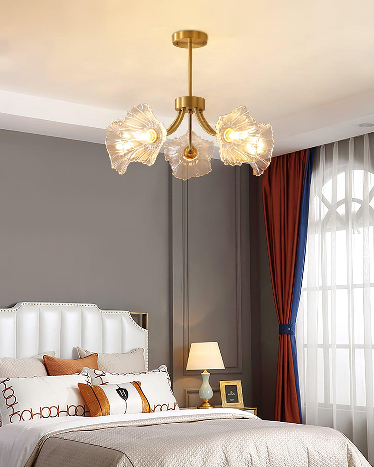 In a grey bedroom with a striped curtain and a lit bedside lamp, this Clérachic chandelier's petal shades glow softly.