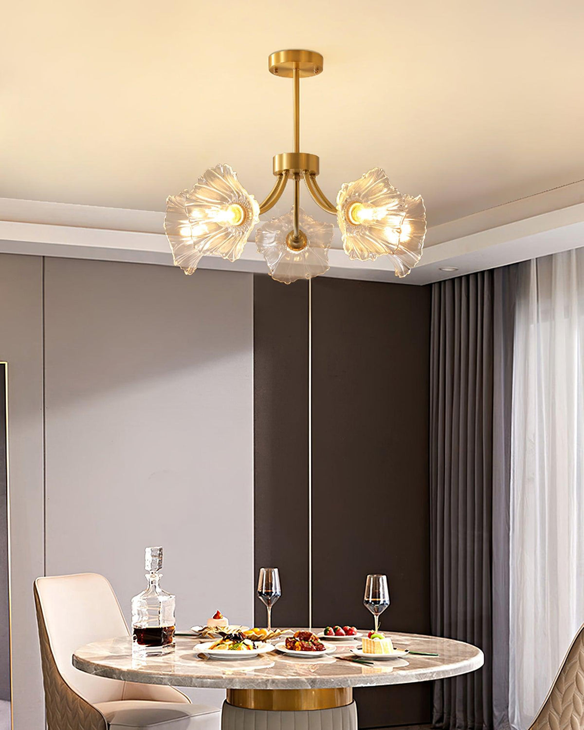 Wine glasses and a decanter sit on a table set beneath this Clérachic chandelier against a plain grey wall.