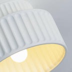 Pleated resin ceiling light glowing softly against a wall