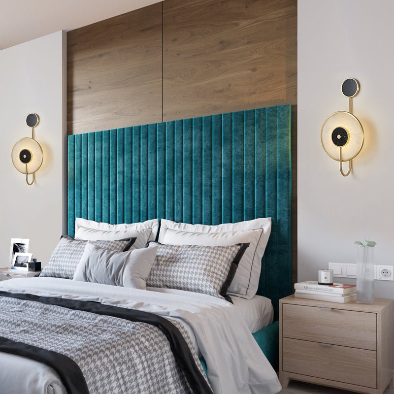 A pair of the sconces lit either side of a teal velvet headboard under wood panelling.