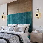 A pair of the sconces lit either side of a teal velvet headboard under wood panelling.