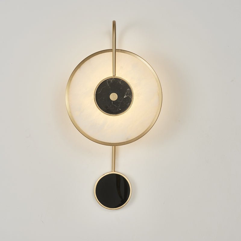 The fixture straight on against pale grey, brass ring around the lit alabaster disc.