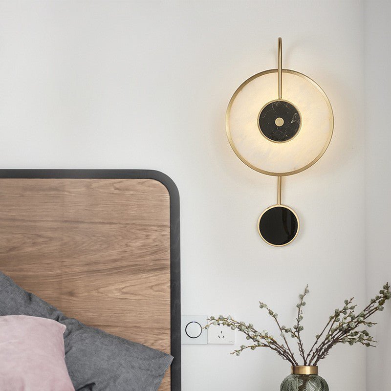 Lit above a walnut bed with a pink cushion, blossom stems in a glass vase alongside.