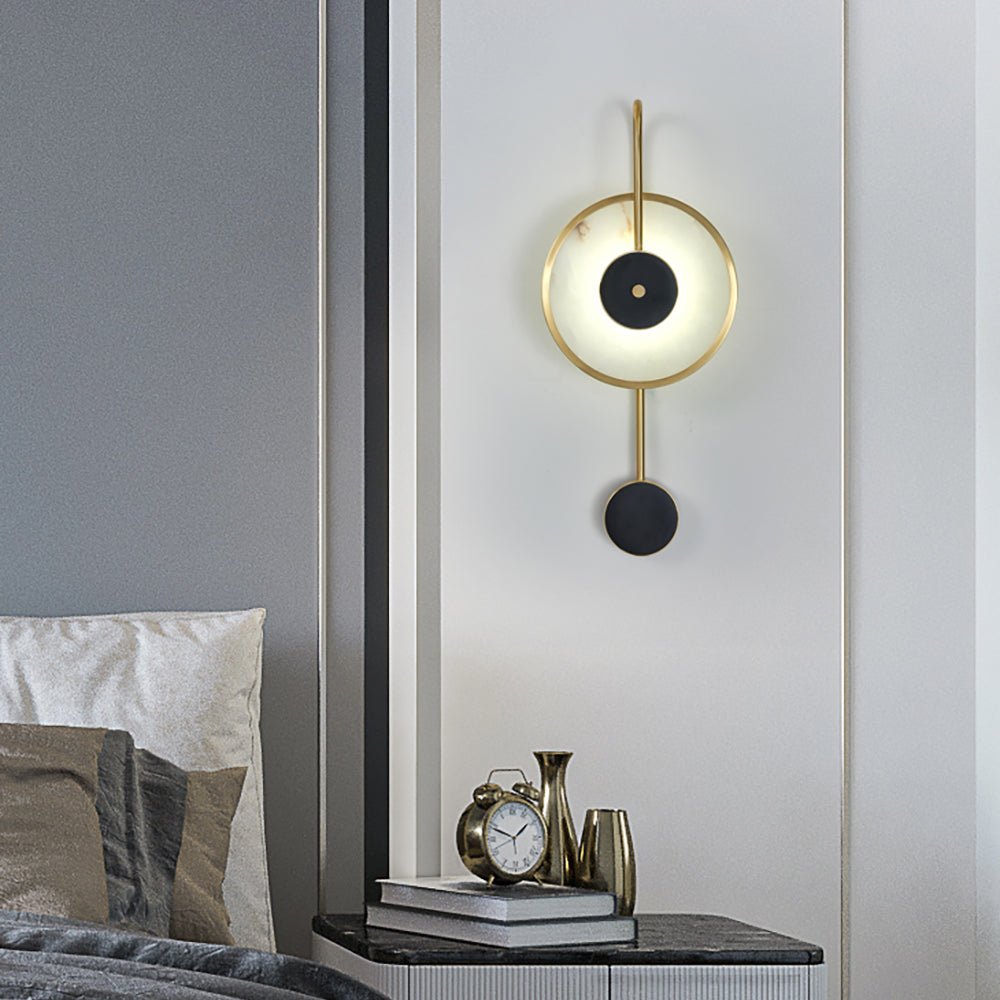 Lit on a white bedroom wall, a brass clock and small vases on the black nightstand below.