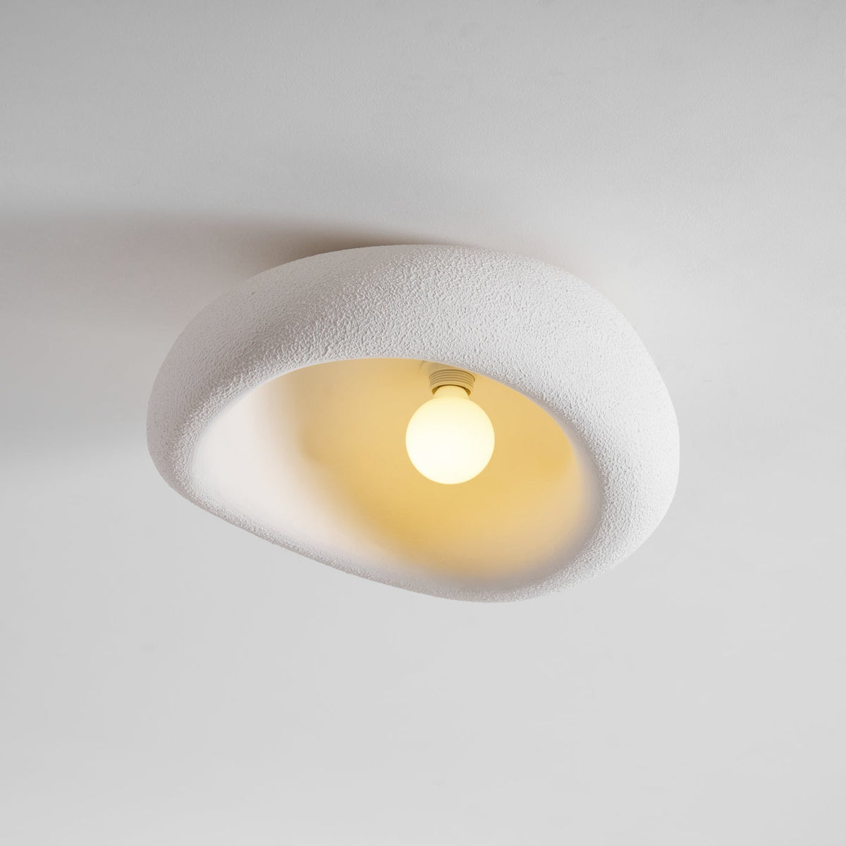 Seen from the front, this Clérachic ceiling light glows around its bulb against a plain grey background.