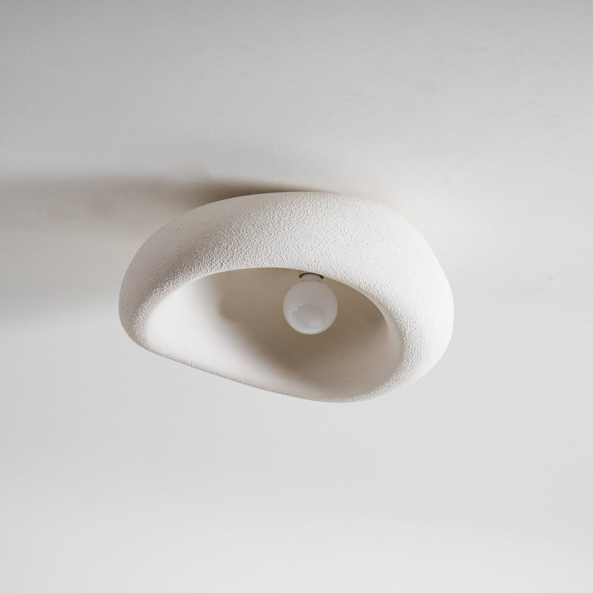 Shown from the front with its plain white bulb visible, this Clérachic ceiling light is unlit against a grey background.
