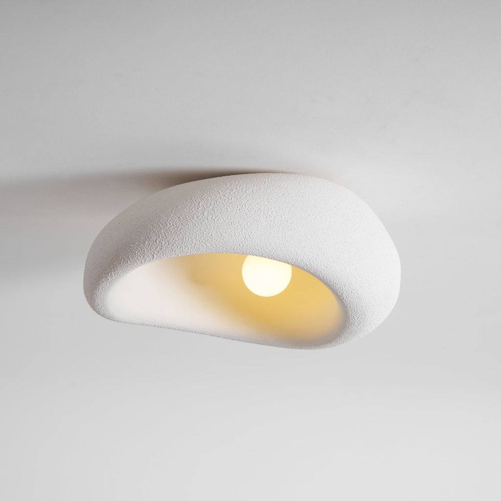 The bouclé-like texture of this Clérachic ceiling light is lit around a glowing bulb, plain grey background.
