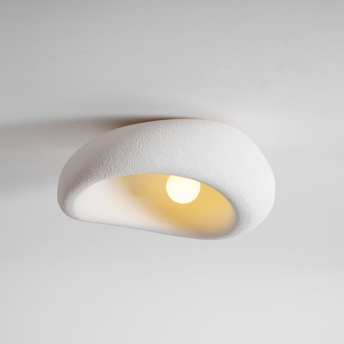 The bouclé-like texture of this Clérachic ceiling light is lit around a glowing bulb, plain grey background.
