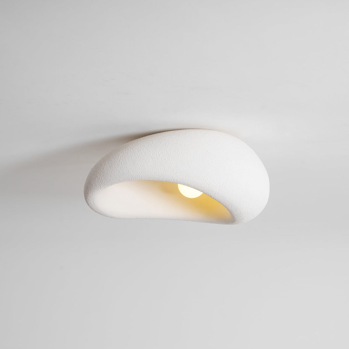 Close view of this Clérachic ceiling light lit against a plain grey background, its bulb glowing beneath the curve.