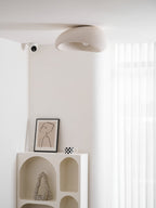 In its white texture finish, this Clérachic ceiling light sits lit near a sheer curtain above a framed sketch and a mug.