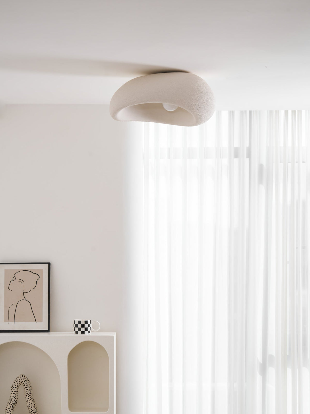 This Clérachic ceiling light glows above a framed line drawing and a chequered mug, sheer curtain behind.