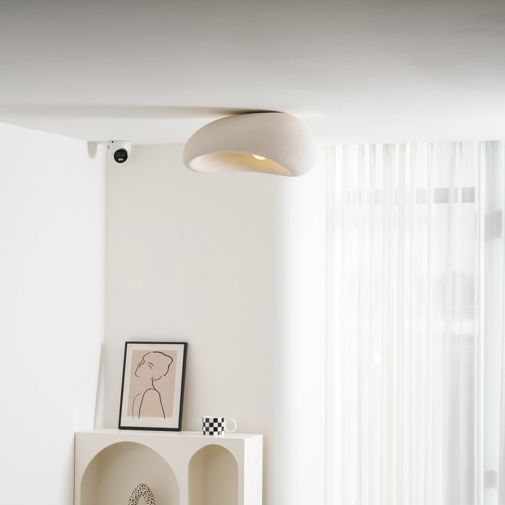 A closer view shows this Clérachic ceiling light lit above a bookshelf and framed sketch near a sheer curtain.