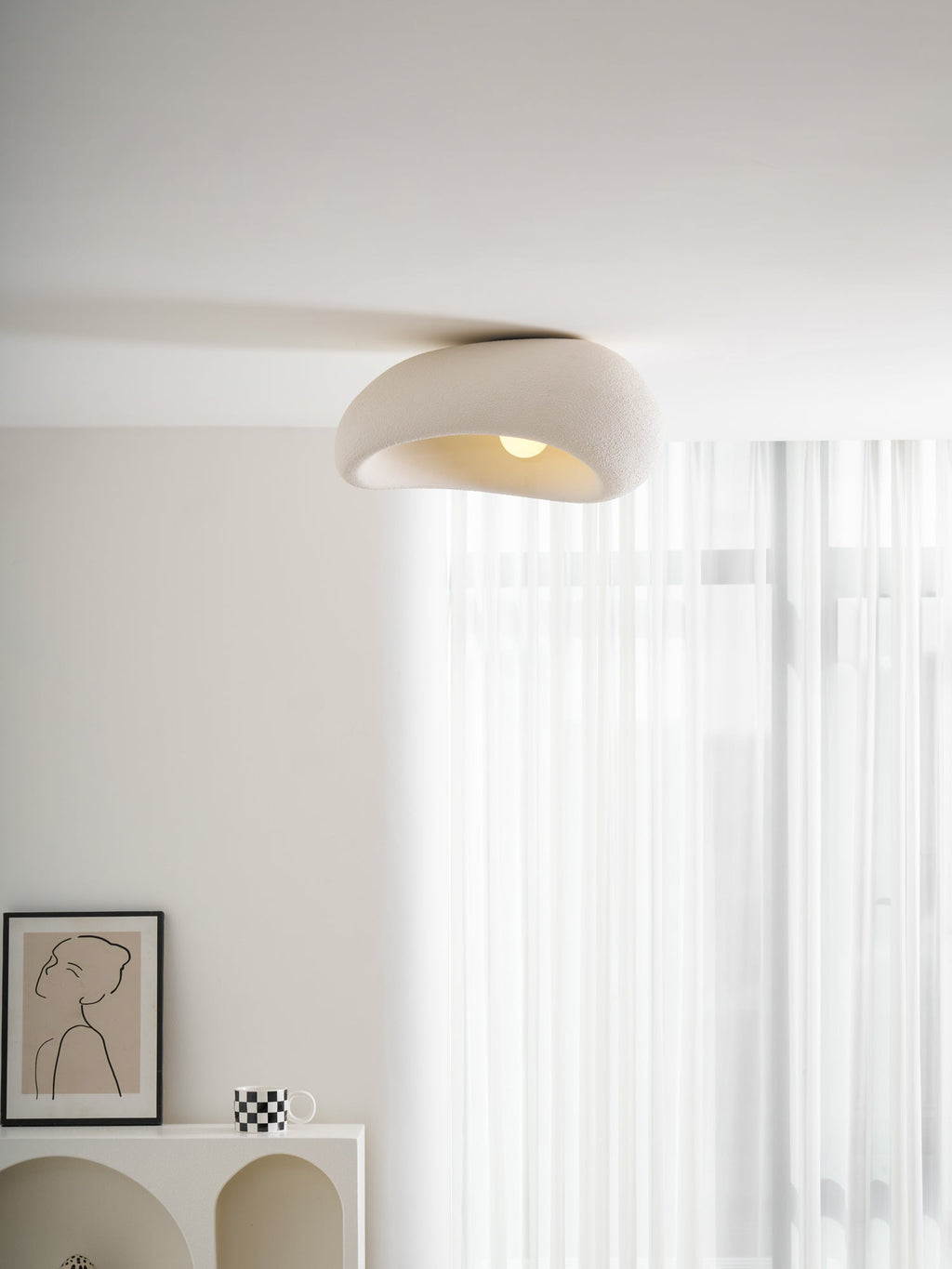 Glowing in a plain corner, this Clérachic ceiling light sits above a curtain and the edge of a framed print.