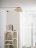 Above a bookshelf holding a framed line drawing and a chequered mug, this Clérachic ceiling light glows in white texture.