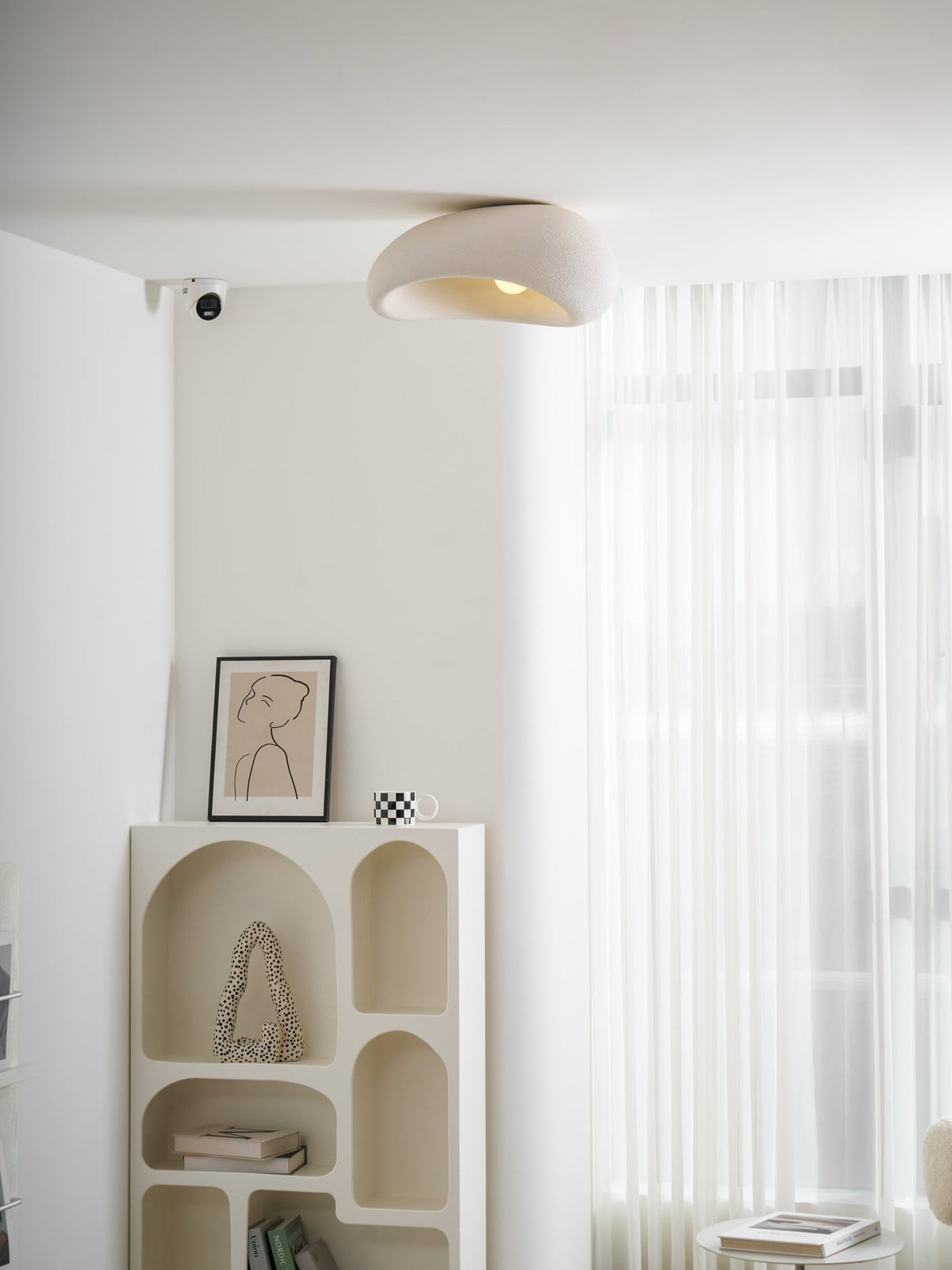 Above a bookshelf holding a framed line drawing and a chequered mug, this Clérachic ceiling light glows in white texture.