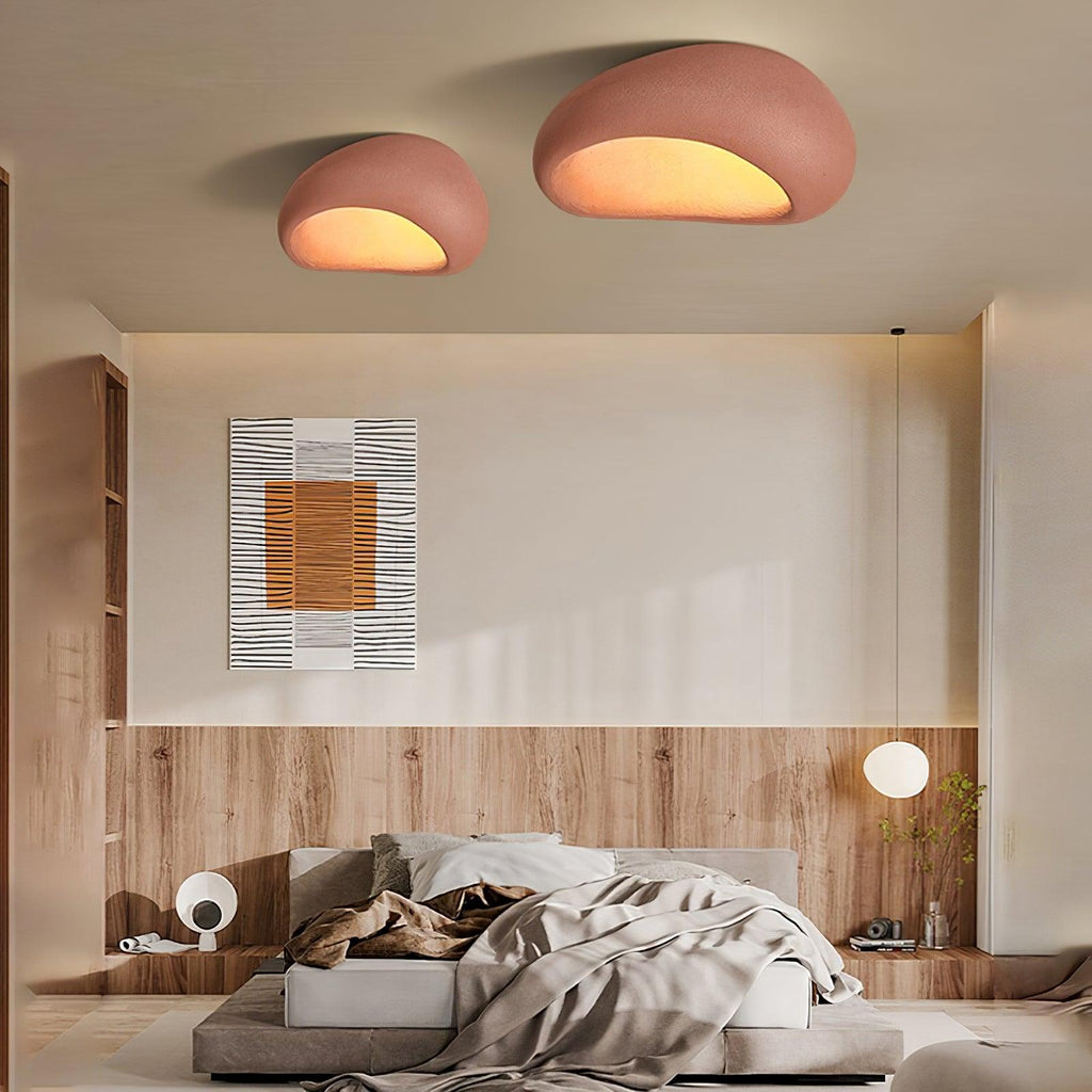 Two of these Clérachic ceiling lights in brick red glow above a bed with an art print and a ring pendant lamp.