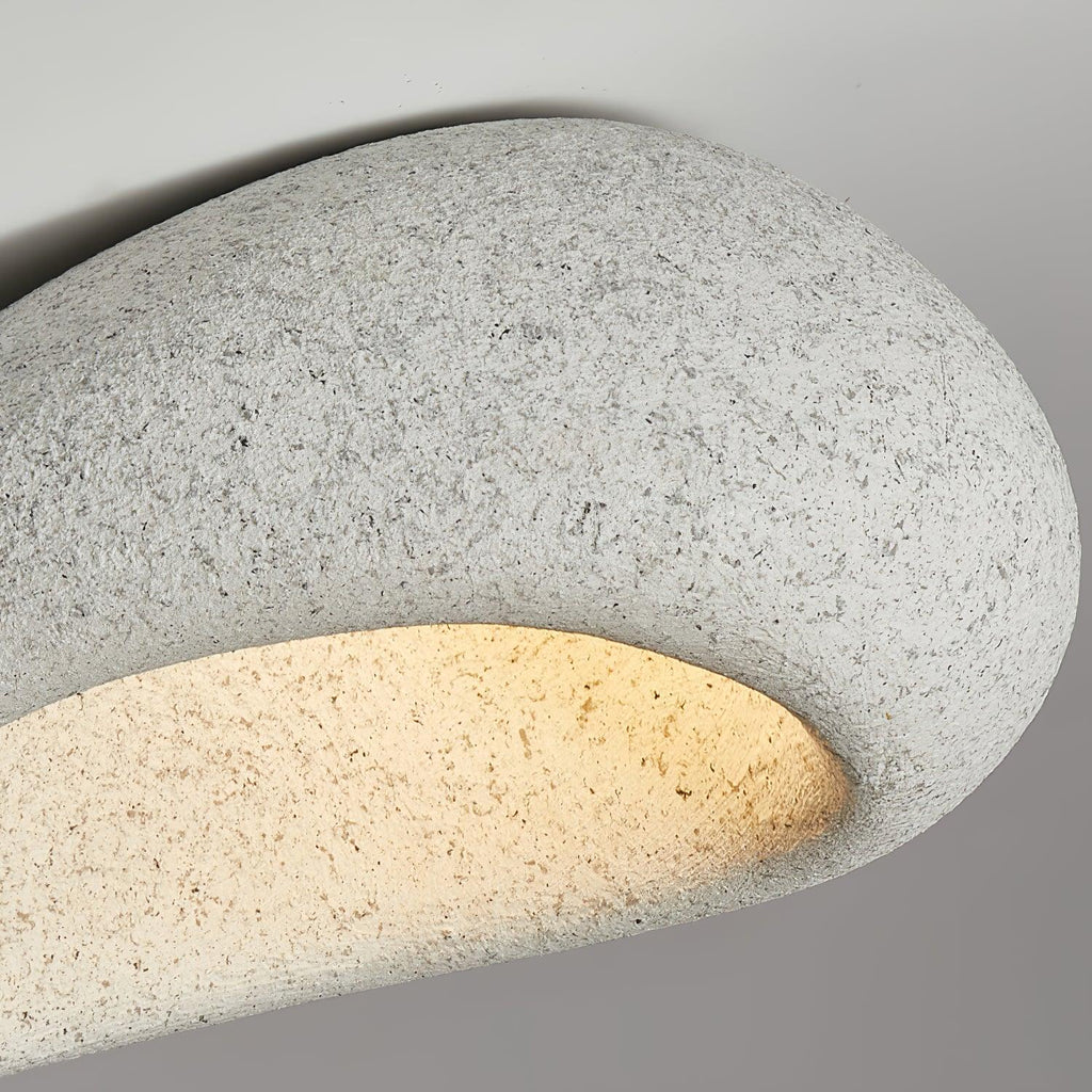Extreme close-up of the speckled stone texture on this Clérachic ceiling light, its underside glowing warmly.