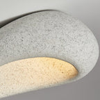 Extreme close-up of the speckled stone texture on this Clérachic ceiling light, its underside glowing warmly.