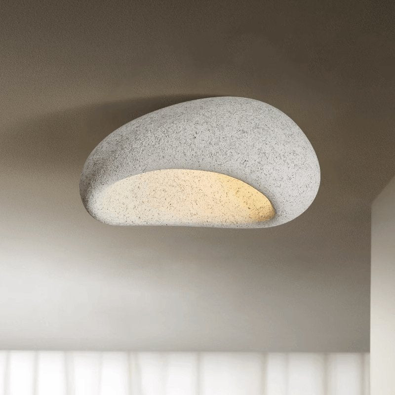 A light speckled stone finish glows on this Clérachic ceiling light, set against a shadowed studio backdrop.