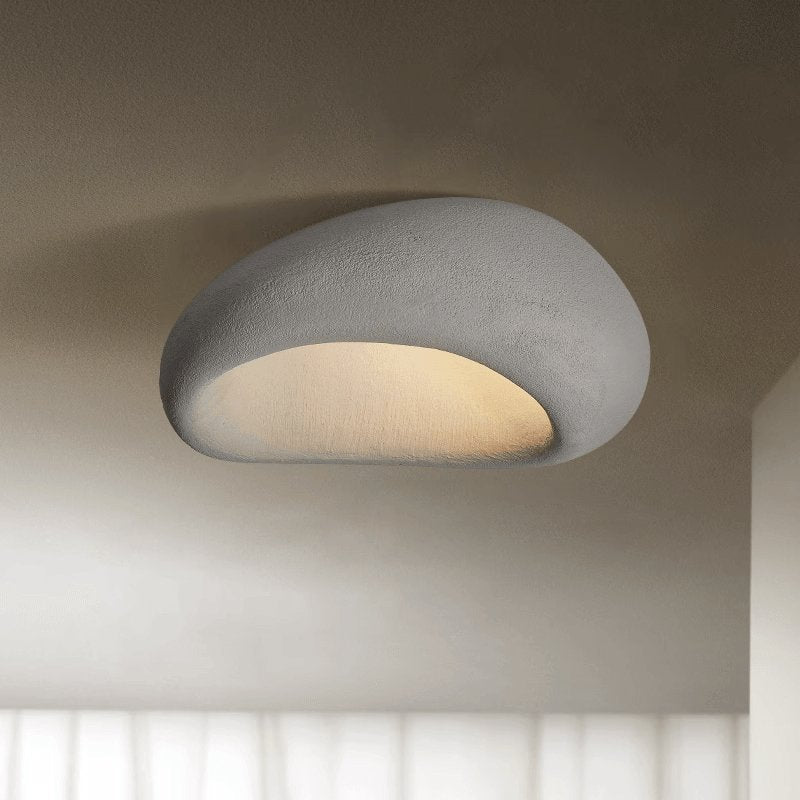 In a cement-grey finish, this Clérachic ceiling light glows against a shadowed studio backdrop.