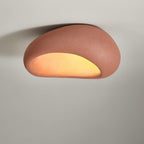In brick red, this Clérachic ceiling light glows against a plain grey wall.
