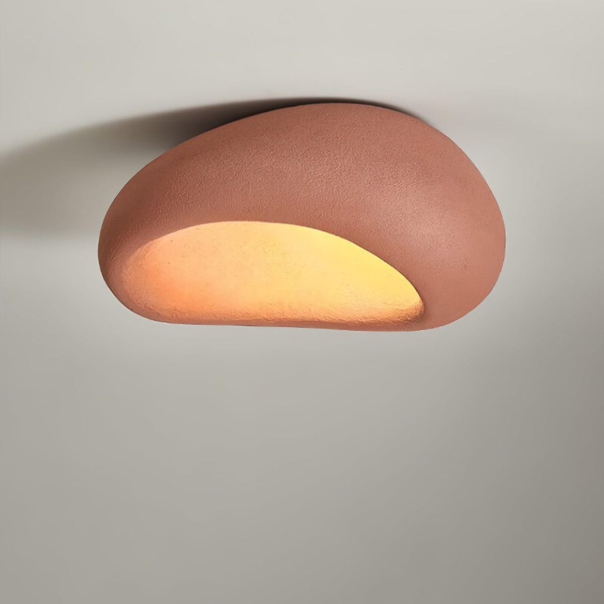 In brick red, this Clérachic ceiling light glows against a plain grey wall.