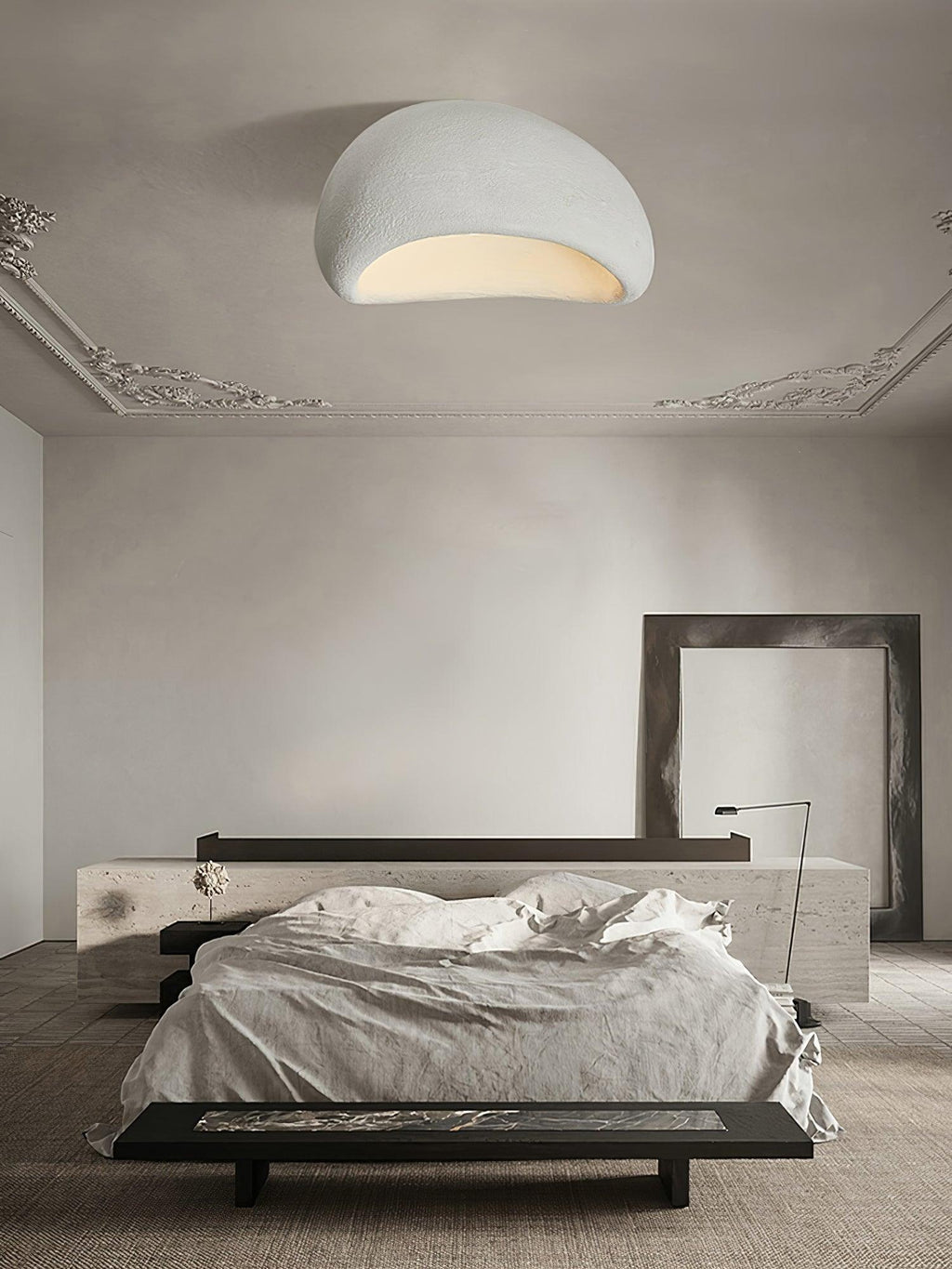 Beneath ornate cornice moulding, this Clérachic ceiling light glows in a pale finish above a dark bench and bed.