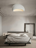 Beneath ornate cornice moulding, this Clérachic ceiling light glows in a pale finish above a dark bench and bed.