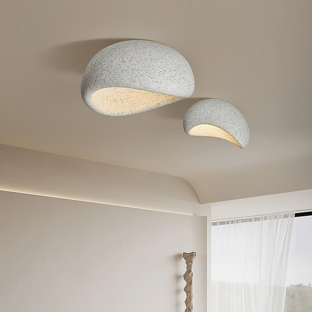 In a speckled grey finish, this Clérachic ceiling light hangs lit near sheer curtains and a carved wood sculpture.