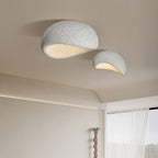 In a speckled grey finish, this Clérachic ceiling light hangs lit near sheer curtains and a carved wood sculpture.