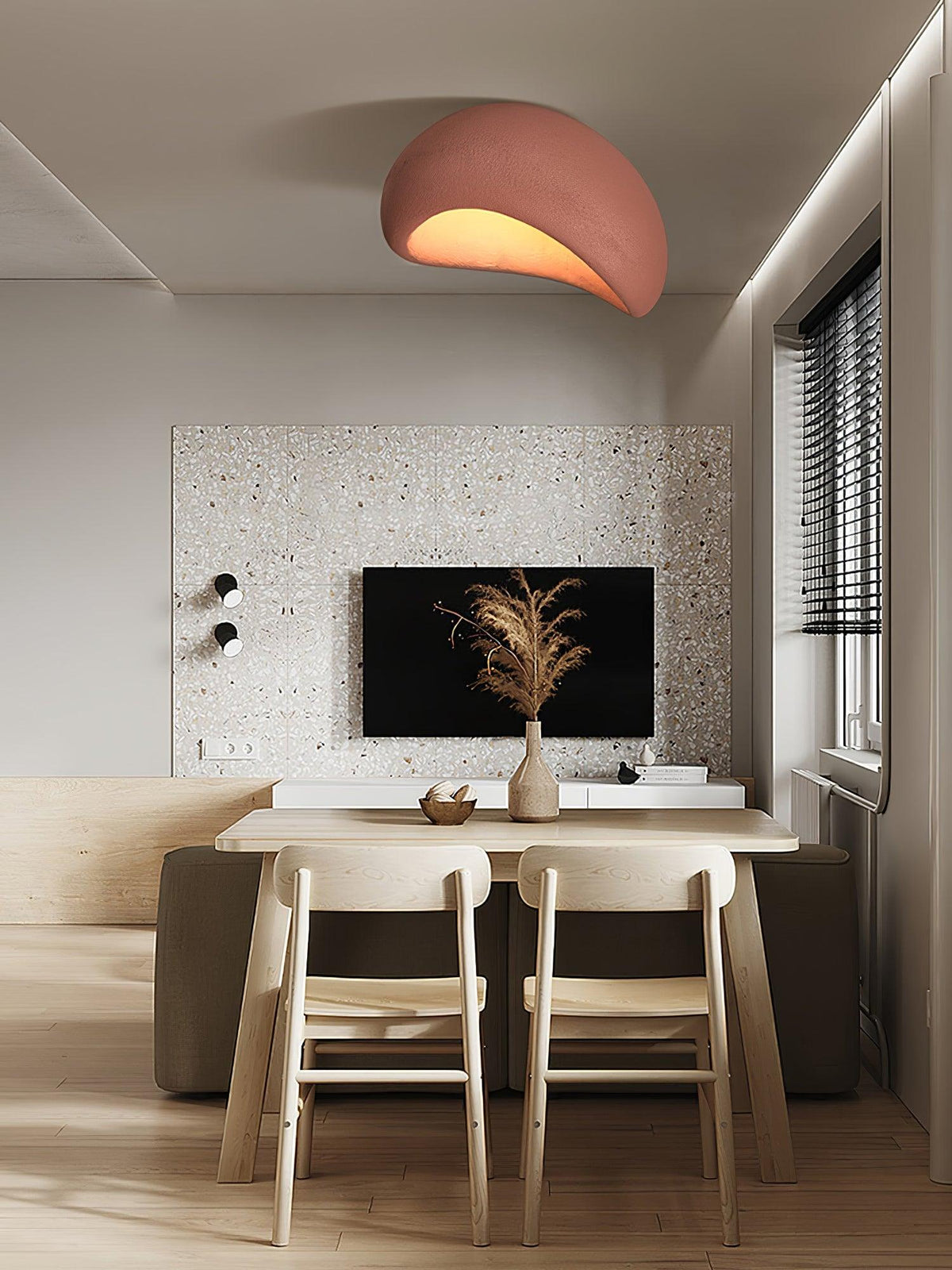 Near a terrazzo wall, this Clérachic ceiling light glows in brick red above a wood dining table set for two.
