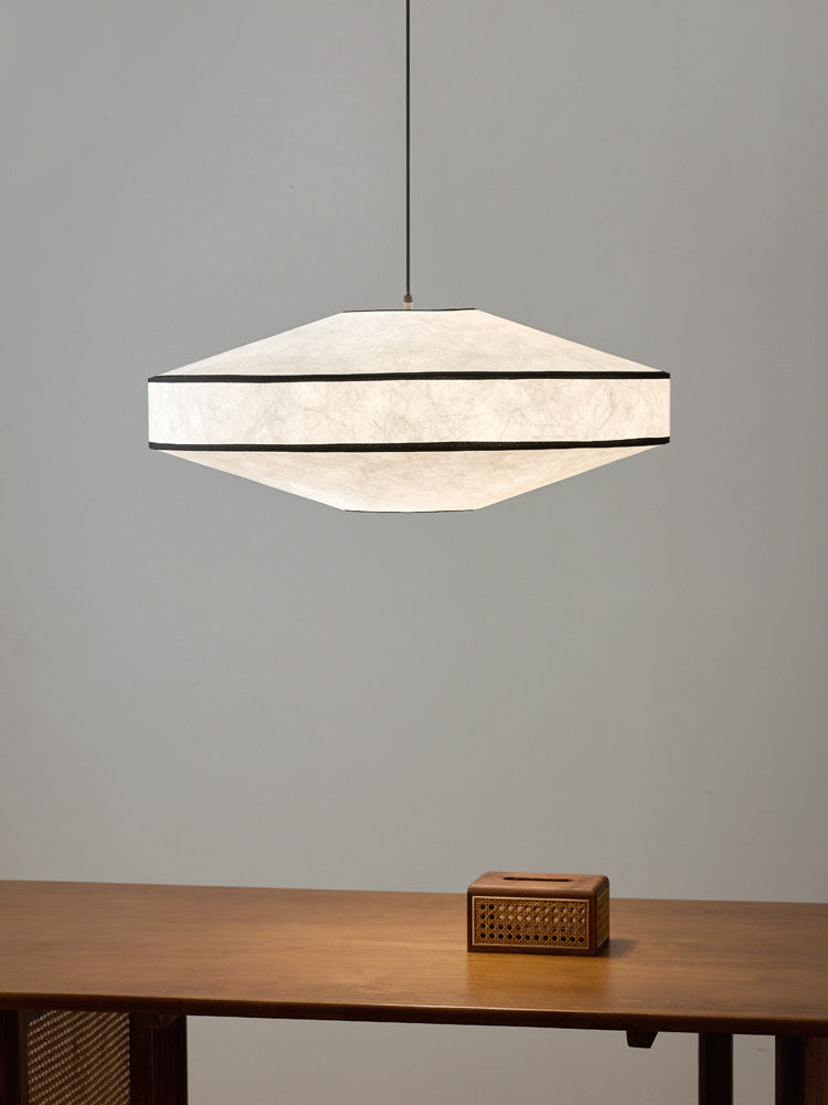 A small woven box sits on a console table below this Clérachic pendant, glowing against a plain grey wall.