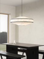 Daylight streams through a tall window onto a black dining table beneath this glowing Clérachic pendant.