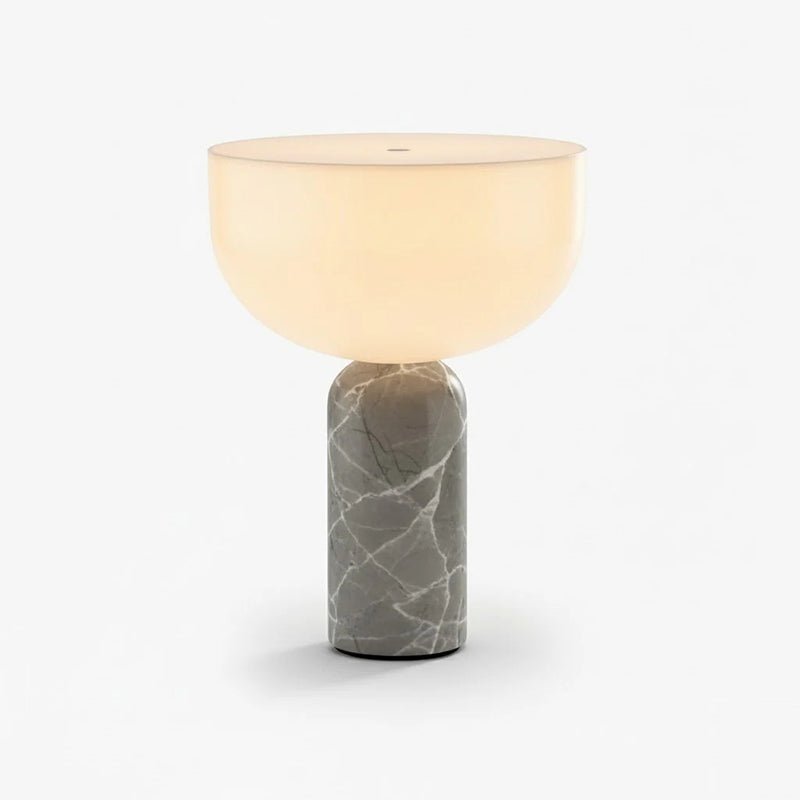 Clérachic table lamp for a console table, its glowing white dome shade sitting atop a grey-veined marble column, photographed on a plain background.