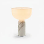 This Clérachic sphere table lamp in pale cream marble, lit and photographed against a plain light grey background.