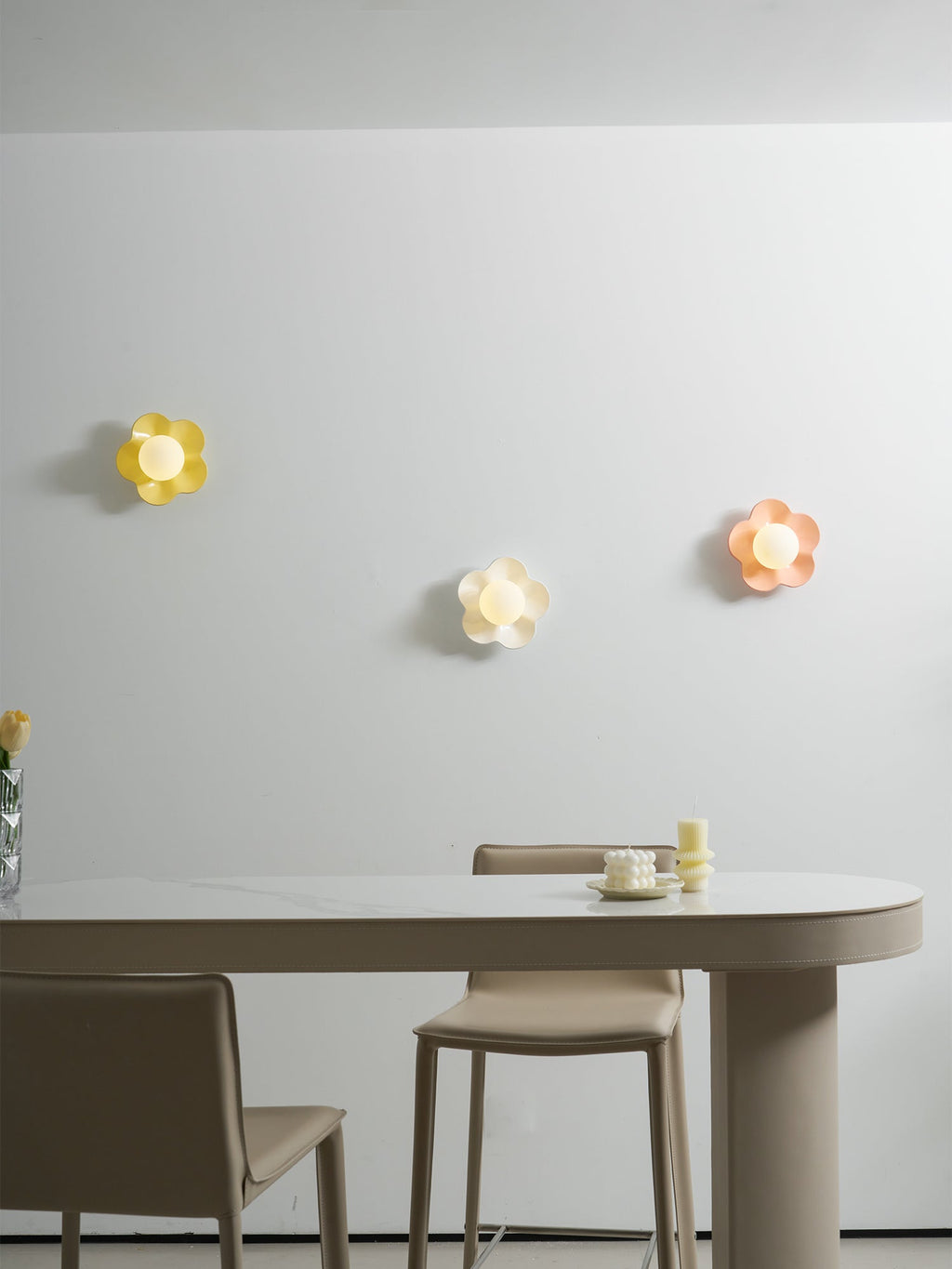 Three of these Clérachic wall lights glow softly above a dining table, in yellow, white and pink.