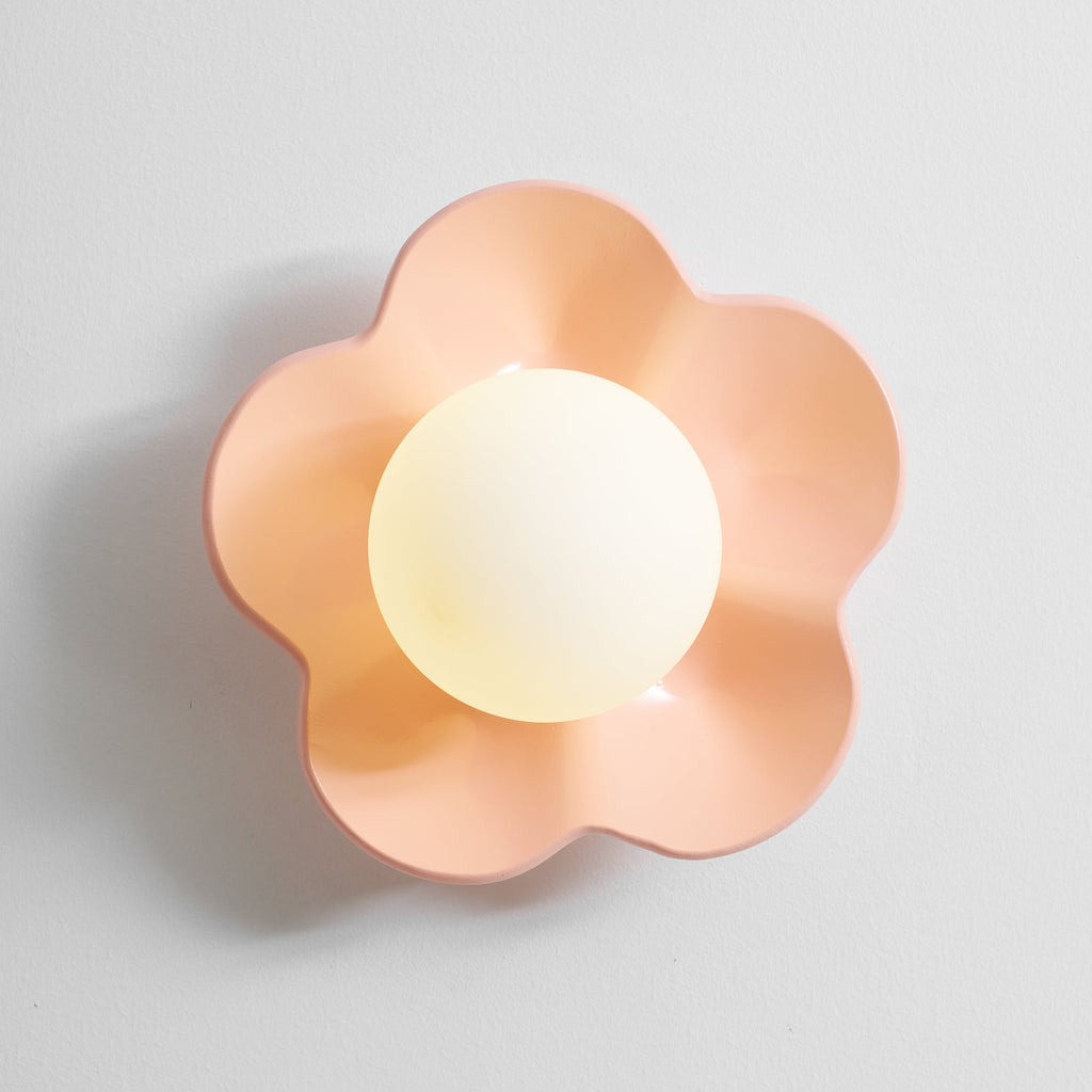 Close studio shot of this Clérachic wall light in pink with its ball lit, against a plain grey backdrop.