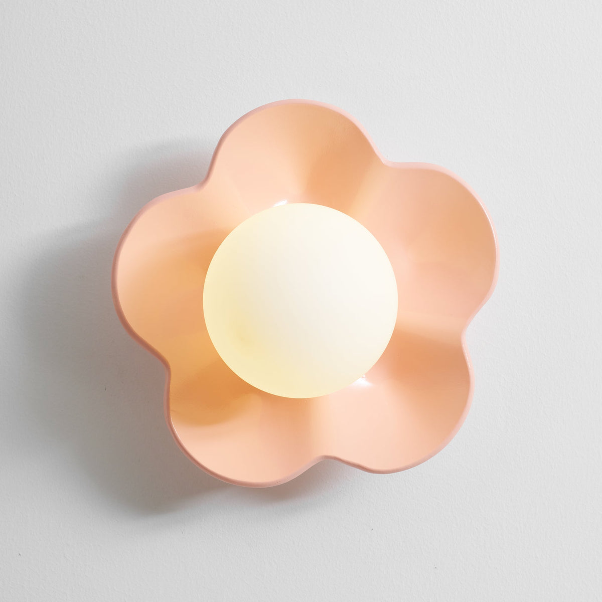 Close studio shot of this Clérachic wall light in pink with its ball lit, against a plain grey backdrop.