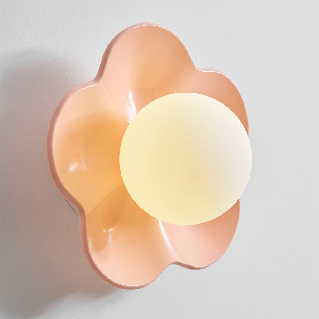 Photographed at a slight angle, this Clérachic wall light in pink glows against a plain grey backdrop.