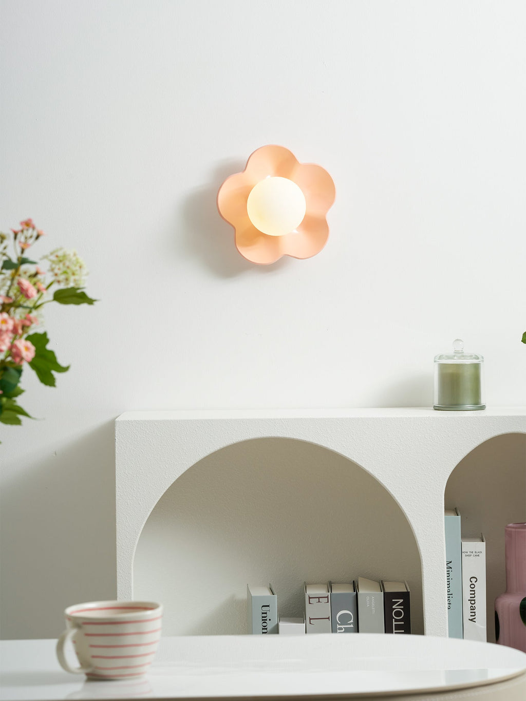 Mounted high above a curved console table with books and a cup, this Clérachic wall light in pink glows softly.