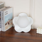 Standing unlit beside a stack of books and a small candle, this Clérachic wall light in white sits on the table.