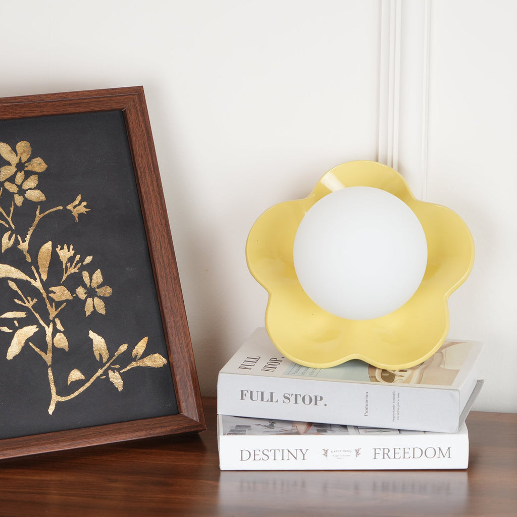 Beside a framed gold botanical print, this Clérachic wall light in yellow stands unlit on a stack of books.