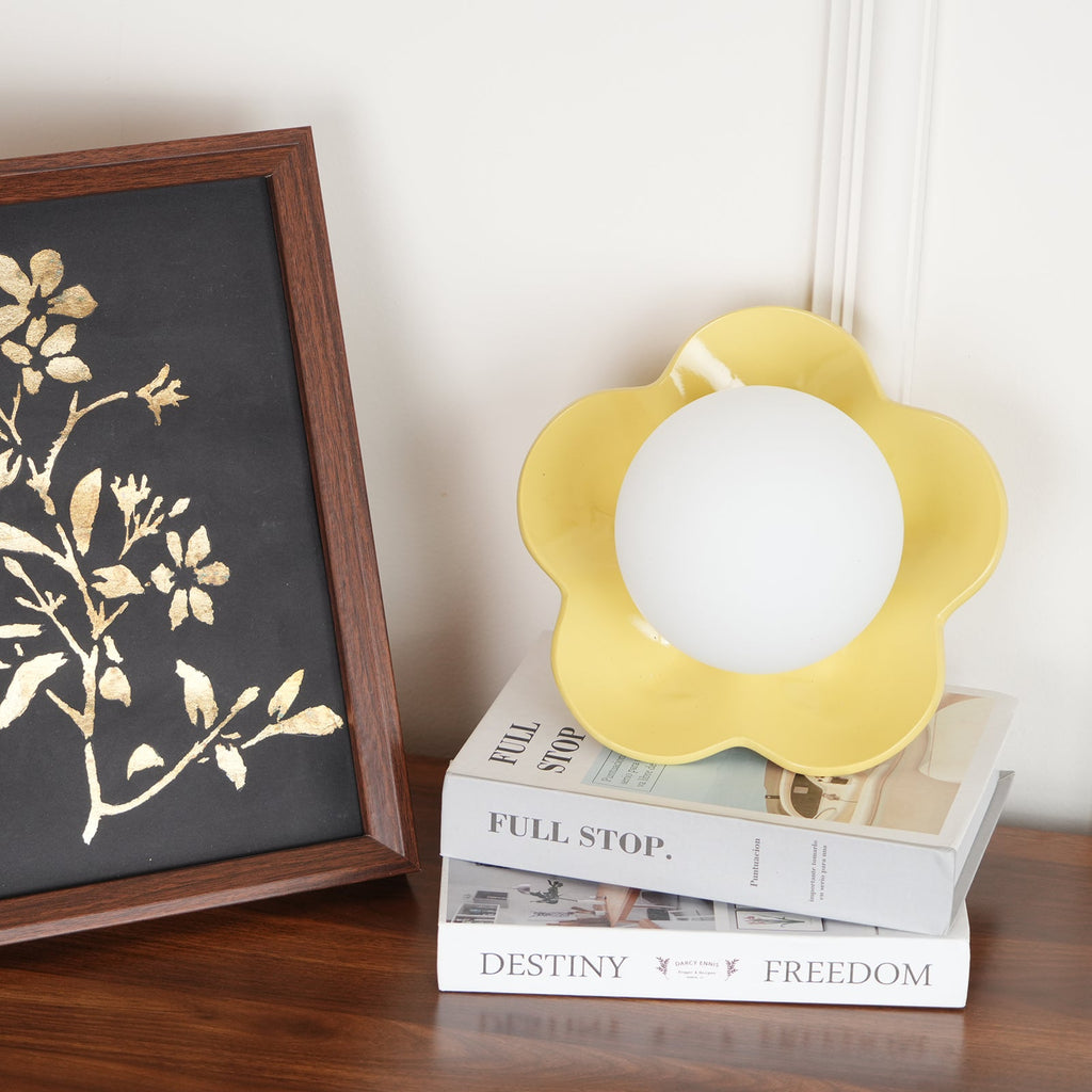 A smaller, more distant view of this Clérachic wall light in yellow, standing on books beside a framed print.