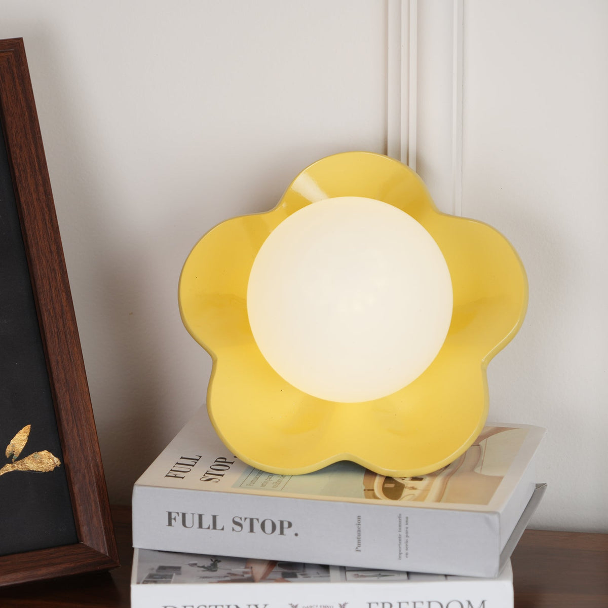 Beside a black-framed print, this Clérachic wall light in yellow stands unlit on a stack of books.